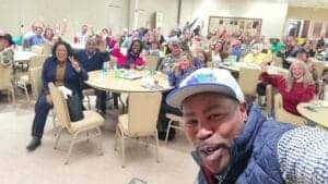 Diverse group of people smiling and waving at a community event, showcasing engagement and camarader.