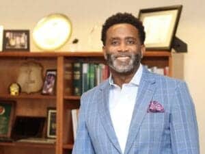 African American businessman in a blue checkered suit smiling in a professional office environment.
