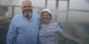 Elderly couple smiling and enjoying time together in a greenhouse setting, showcasing happiness and.