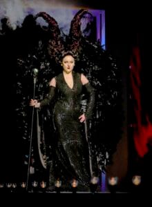 Glamorous woman in black gown with elaborate feathered headpiece on runway show.