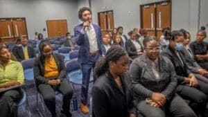 Engaged man asking question at conference with diverse audience.