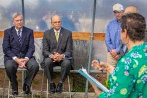 Planting event with officials and a woman in a floral shirt discussing environmental initiatives.