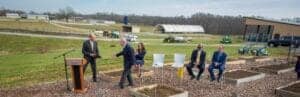 Business leaders shaking hands outdoors at a groundbreaking ceremony.
