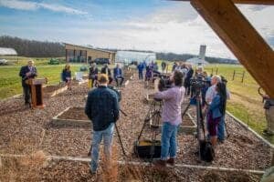Elevated outdoor event with speakers, media crew, and attendees at a community gathering or press co.