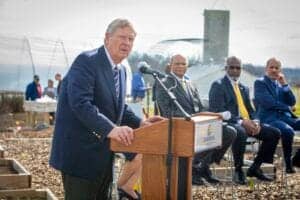 Businessman speaking at outdoor press conference with officials in formal attire.