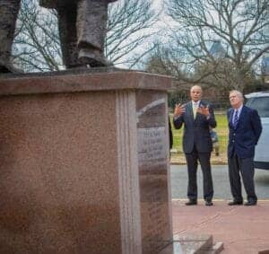 A detailed view of two men in suits discussing near a monument with a statue on top, outdoors in a p.