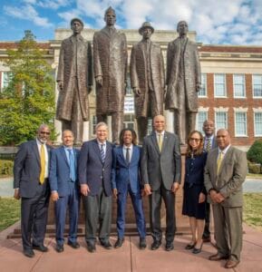 Empowered diverse leaders standing in front of a historic monument with statues of prominent figures.