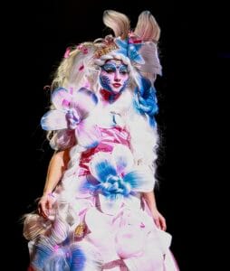 Brightly colored performer in elaborate floral costume with vibrant makeup and headpiece at a fashio.