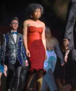 Elegant woman in a red strapless dress at a formal event with other well-dressed attendees.