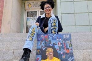 Diverse student sitting on school steps with a colorful CAES News tote bag.