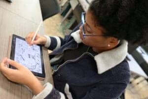 A woman using a tablet and stylus to create digital art or take notes in a classroom setting.