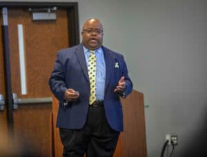 Professional male speaker in a blue suit delivering a presentation at a conference.