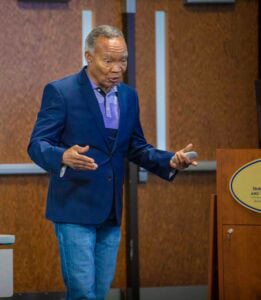 An elderly man speaking passionately at a conference or seminar.