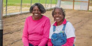 Enjoying gardening outdoors with two smiling women in a greenhouse or garden setting.