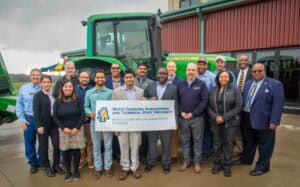 Agricultural professionals holding a North Carolina A&T banner outdoors with farm equipment in backg.