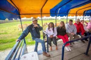 Enjoying a guided tour on a farm wagon with diverse visitors and scenic rural background.