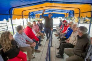 Outdoor educational tour with diverse group seated on a covered boat deck.