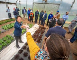 Sustainable agriculture workshop in a greenhouse with diverse participants and a presenter explainin.