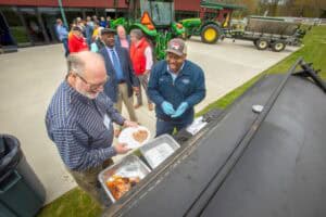 A1. ALT tag: Community event with people serving food outdoors near farm equipment.