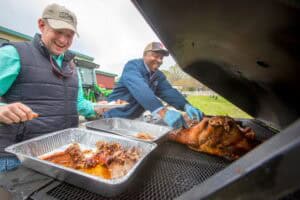 Grilling barbecue outdoors with two smiling men at a community event.
