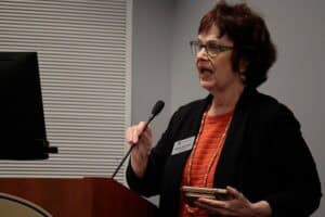 Professional woman speaking at a conference with a microphone and presentation screen.