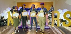 Group of women holding awards at CAES News event with large "NEWS" letters in background.