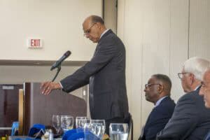 Dignitary delivering speech at formal event with seated audience and table settings.