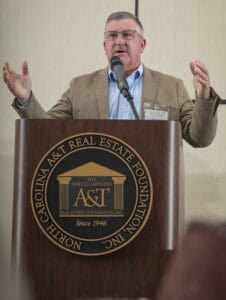 Man speaking at a conference behind a podium with North Carolina Real Estate Foundation logo.