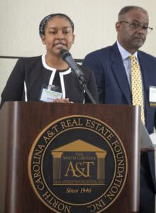 Empowered woman speaking at North Carolina real estate event with a man listening attentively.