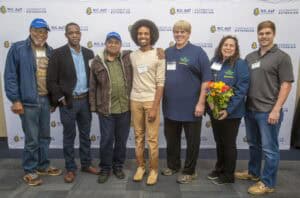 Empowered diverse group of people at CAES News event with NC A&T logo backdrop.
