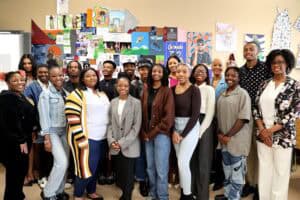 Diverse group of students and teachers in a classroom with colorful artwork on the wall.