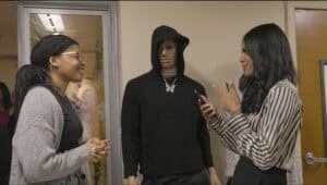 A woman in a striped blouse and a woman in glasses and a gray sweater talking to a mannequin dressed.