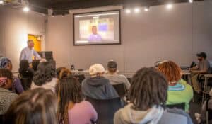 A teacher giving a presentation to a diverse group of students in a classroom setting.