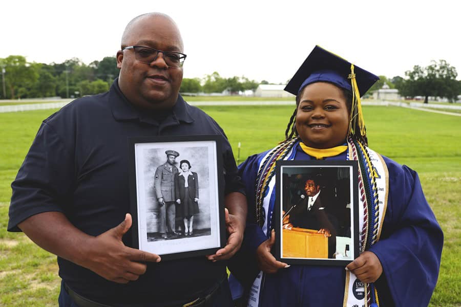 Man and woman celebrating graduation outdoors, holding framed photos.