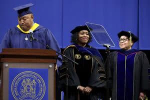 Graduation ceremony with diverse graduates in academic regalia on stage at CAES News event.