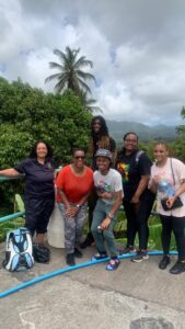 A woman and four girls standing outdoors with lush greenery and palm trees in the background.