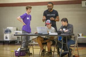 Engaged group of young students and instructor collaborating on a tech project in a gymnasium.