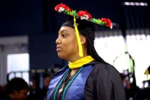 Graduation cap with red and white flowers, woman in academic gown at graduation ceremony.