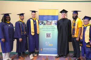 Graduates in academic regalia at a university graduation ceremony with a banner in the background.