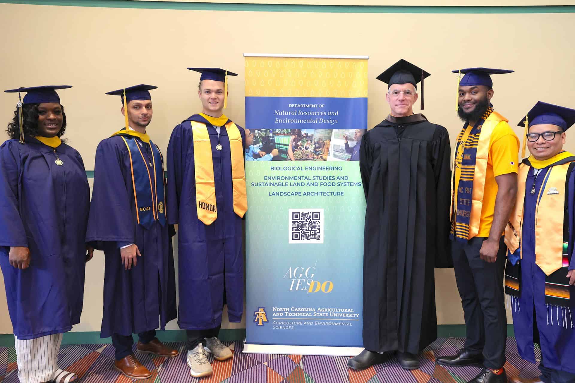 Graduates in academic regalia at a university graduation ceremony with a banner in the background.