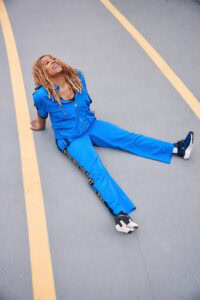 Bright smiling woman in blue sportswear sitting on the road, enjoying outdoor activity and fitness.
