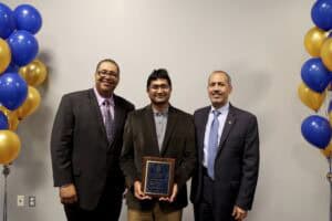 Award recipient with two officials at a formal event, celebrating achievement in a professional sett.