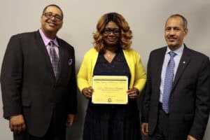 Woman holding diploma with two men in formal attire at an award ceremony.