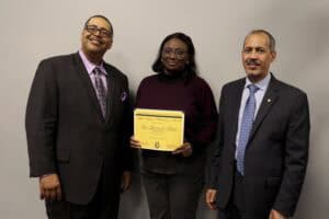 Woman receiving certificate from two men in formal attire at CAES News event.