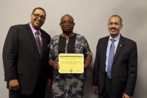 Award recipient holding certificate with two men in formal attire standing beside him.
