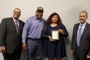 Celebration of achievement with diverse professionals holding award plaque at CAES News event.