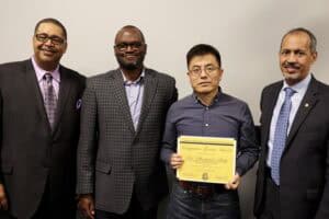 Group of four men at an award ceremony, one holding a certificate, in professional attire.