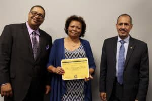 Empowered woman receiving award at formal event with two men in suits.