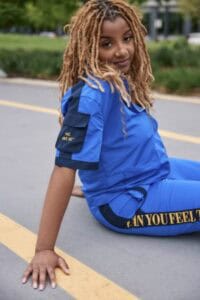A woman with dreadlocks sitting on the street wearing a blue sports outfit.