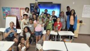Group of diverse students celebrating success in classroom with trophies and smiles.
